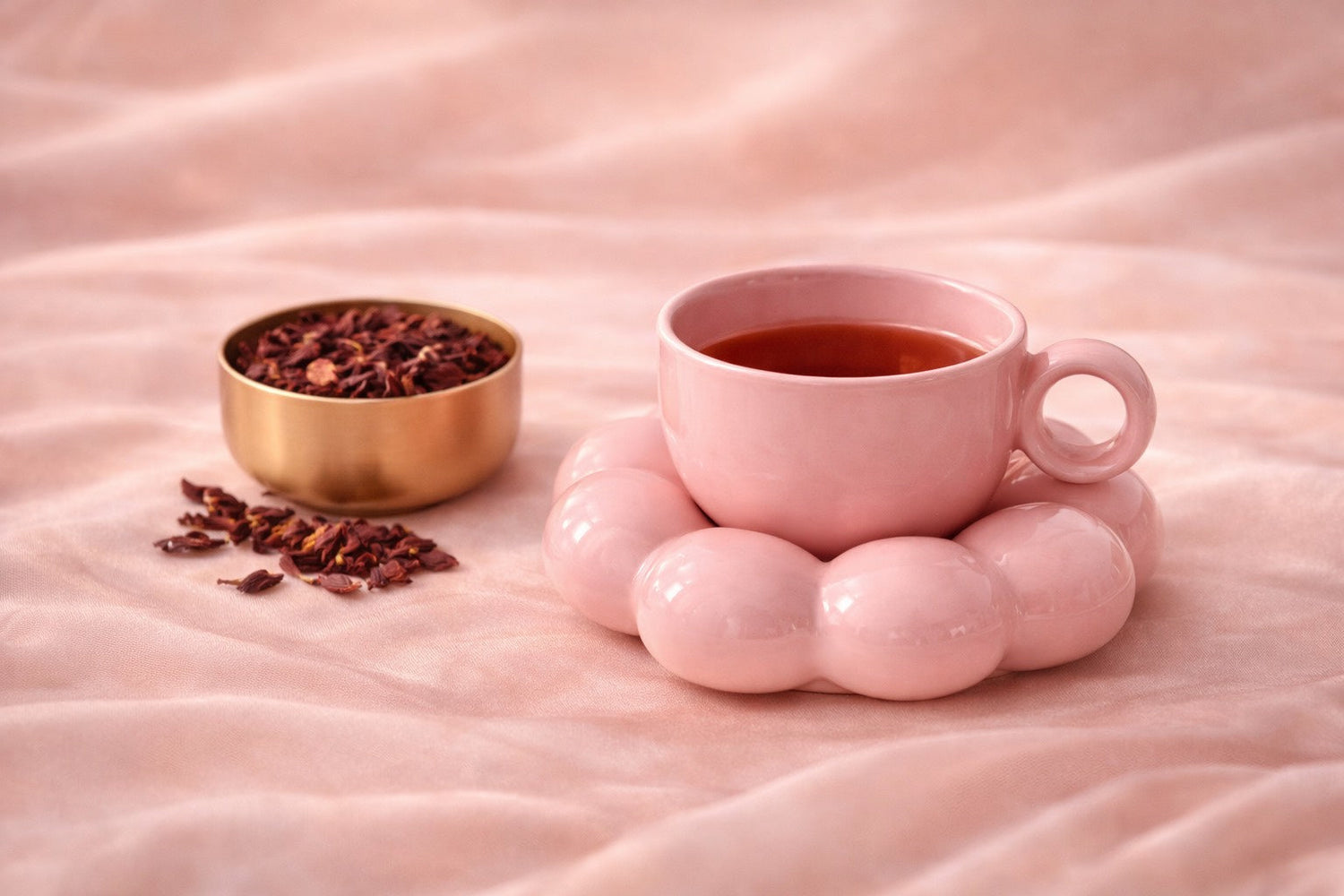 Tasse bubble en céramique rose pâle posée sur un drapé en satin rose poudré, accompagnée d’un petit bol doré et d’une cuillère fine, ambiance douce et féminine Hazellia, style rituel bien-être premium