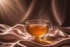 infusion bien-être ambre dans tasse en verre double paroi sur satin rose poudré, ambiance luxe Hazellia, rituel féminin apaisant

