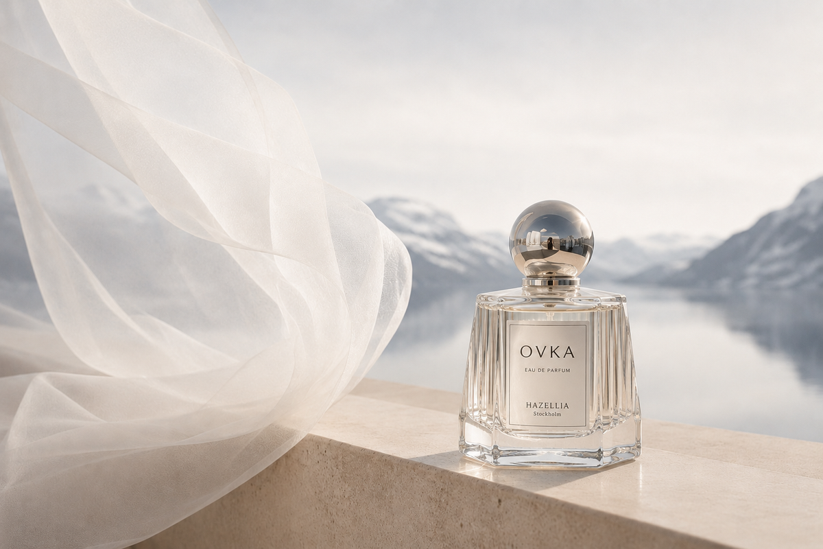 Parfum Ovka Maison Hazellia en flacon cristal et argent face à un fjord scandinave avec voile ivoire aérien – Scandinavie Cocooning


