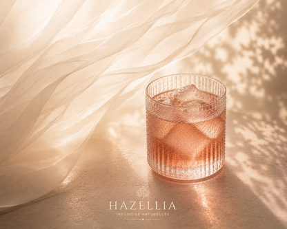Deep Silk Hazellia – infusion glacée rosée ambrée dans un verre cristal premium avec glaçons réalistes, voile ivoire aérien et ambiance slow luxe sur marbre lumineux.

