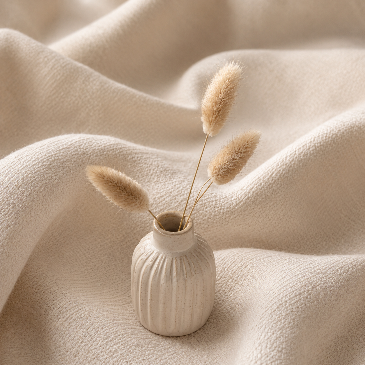 Décoration scandinave minimaliste premium sur tissu ivoire Hazellia Voyage — petit vase céramique beige avec herbes séchées, ambiance cocooning nordique douce et élégante

