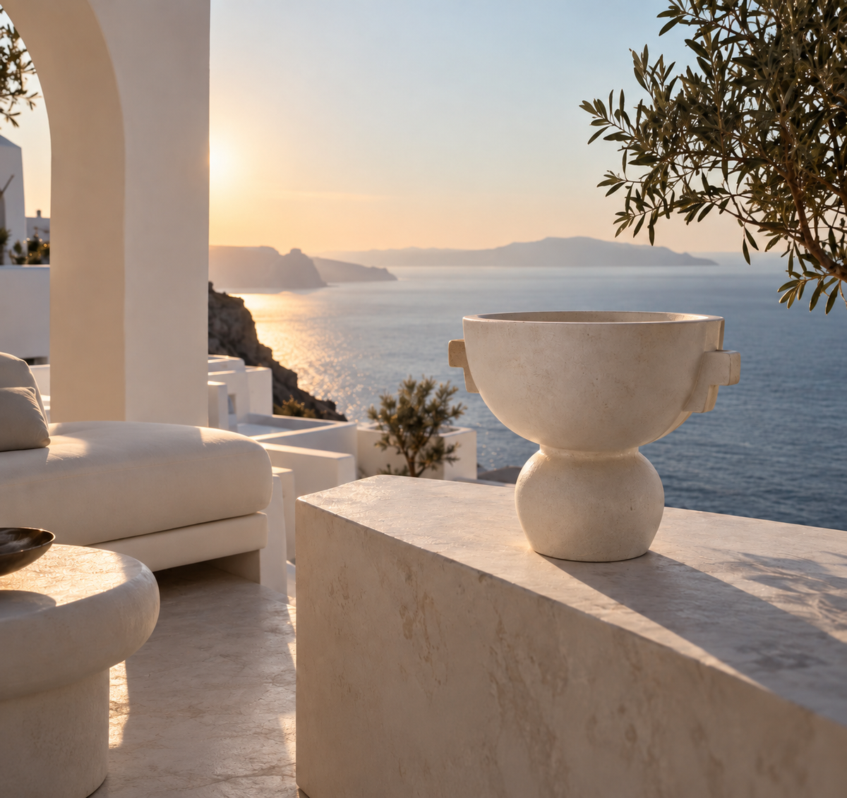 Terrasse grecque contemporaine en pierre ivoire avec vase sculptural, olivier et vue sur la mer Égée au coucher du soleil – Grèce Éternelle Hazellia

